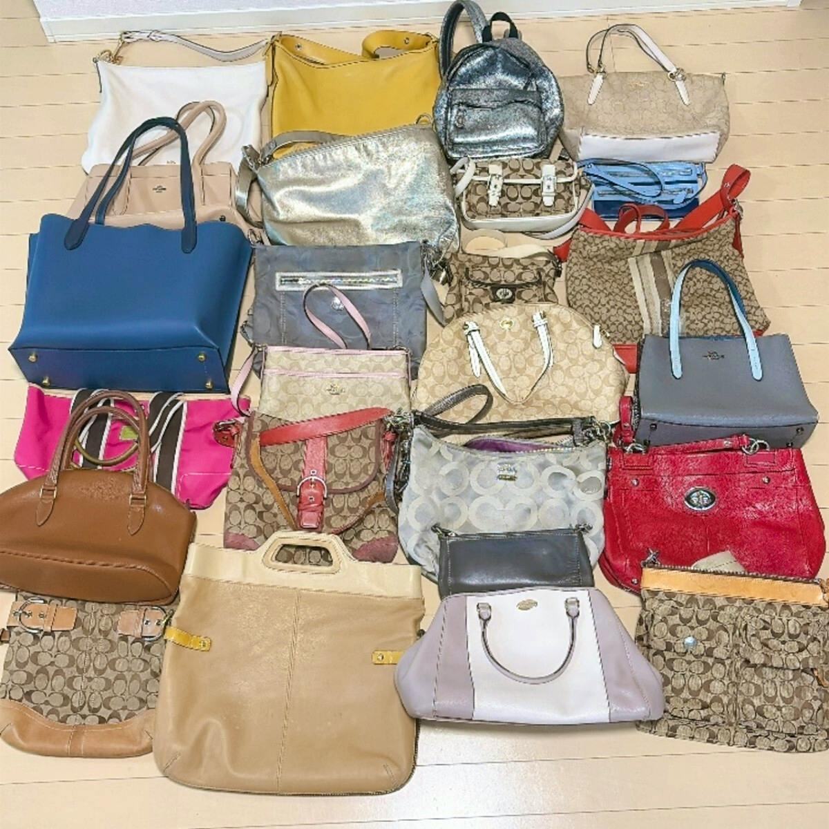 A grouped arrangement of many COACH handbags and totes in assorted colors and signature canvas patterns laid out on a floor as a bulk set.