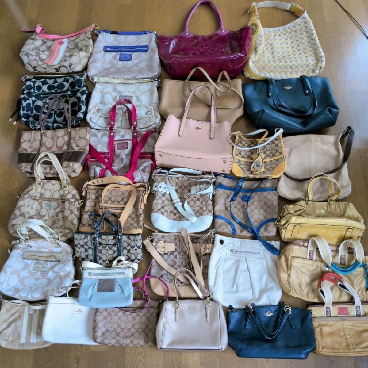 Multiple Coach canvas and leather handbags and totes arranged on a floor as a bulk lot.