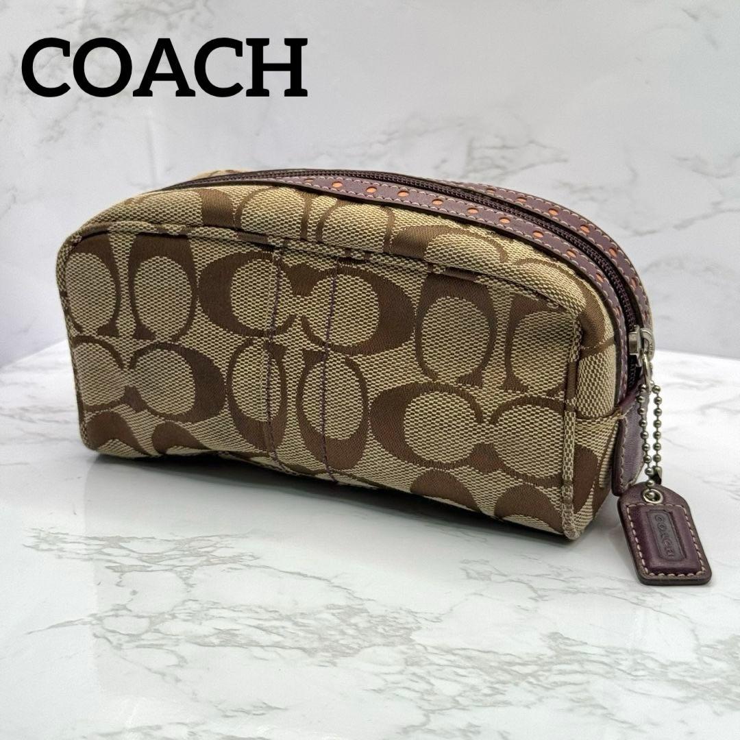Brown Coach signature canvas and leather cosmetic pouch with zipper and leather tag on a marble surface.