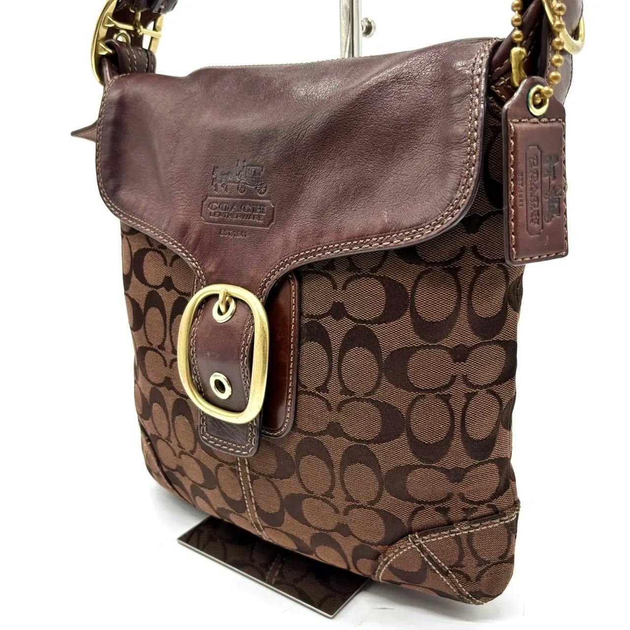 Brown Coach signature canvas shoulder bag with leather flap, brass buckle, and a leather hang tag.