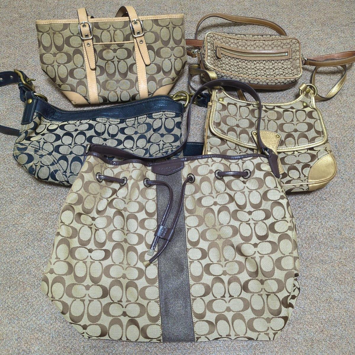 Five COACH signature canvas and leather bags arranged on a carpet, including a large drawstring tote and several smaller shoulder and crossbody bags.
