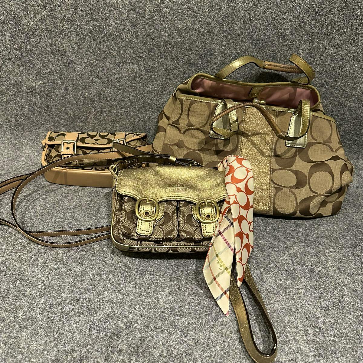 Several COACH signature canvas and leather bags with a patterned scarf arranged on a gray surface.
