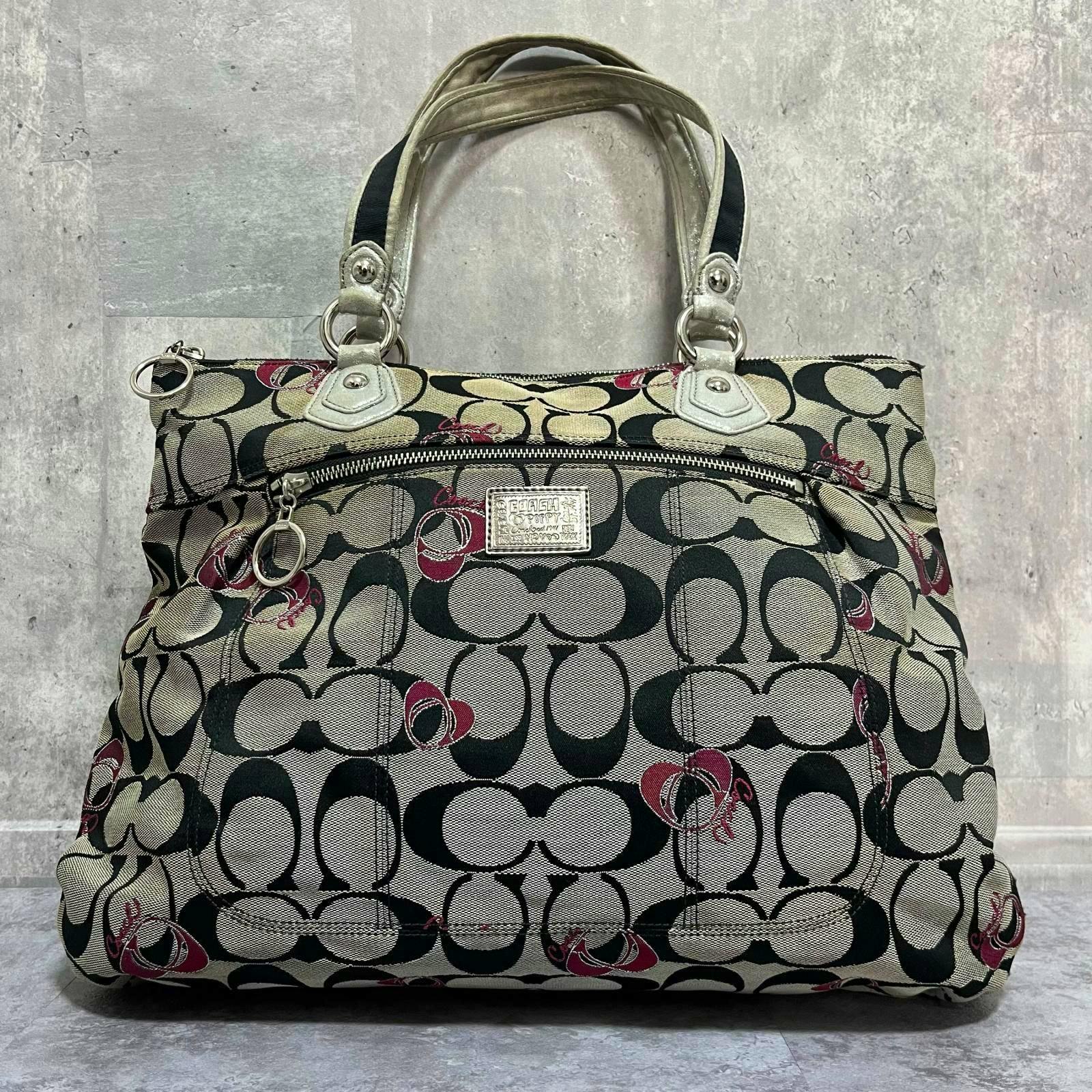 Front view of a Coach canvas signature-pattern tote bag with leather handles and a front zip pocket.