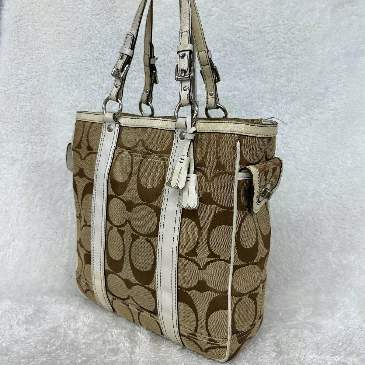 Beige and brown Coach signature-pattern canvas tote bag with white leather trim and double shoulder straps shown upright on a white background.