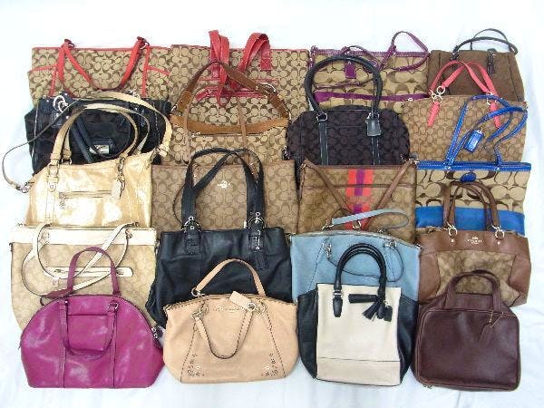 A laid-out assortment of Coach canvas and leather tote, handbag, and shoulder bags from a 20-piece set.