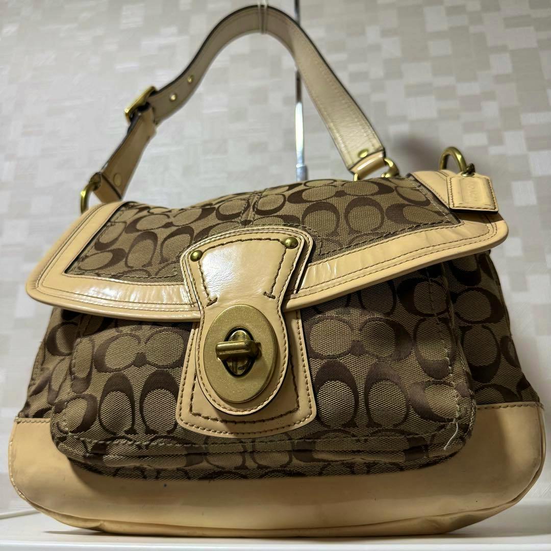 Front view of a Coach shoulder bag in brown signature canvas with beige leather trim and a turn-lock closure.