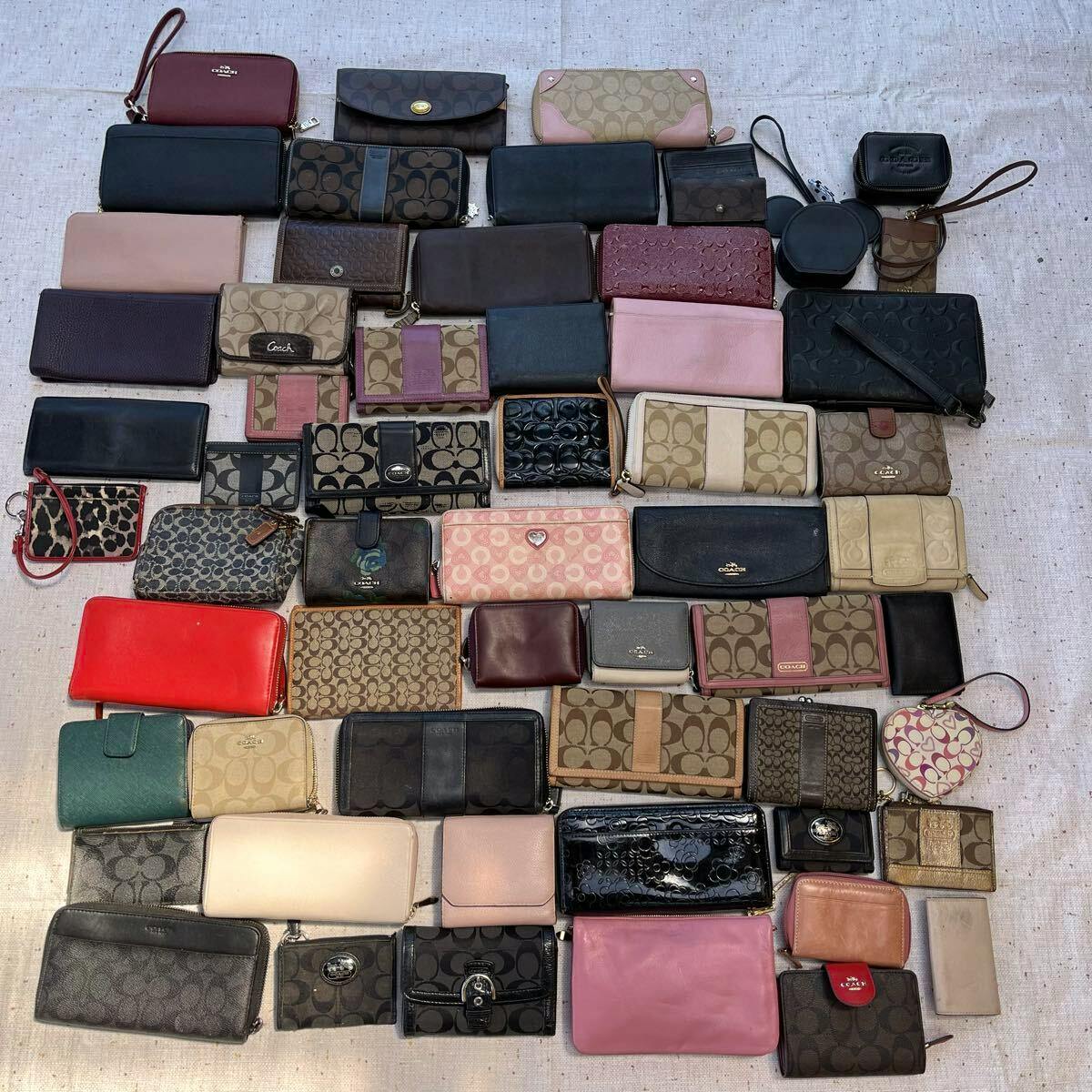 A flat lay of multiple Coach wallets and small accessories arranged in rows on a fabric surface.