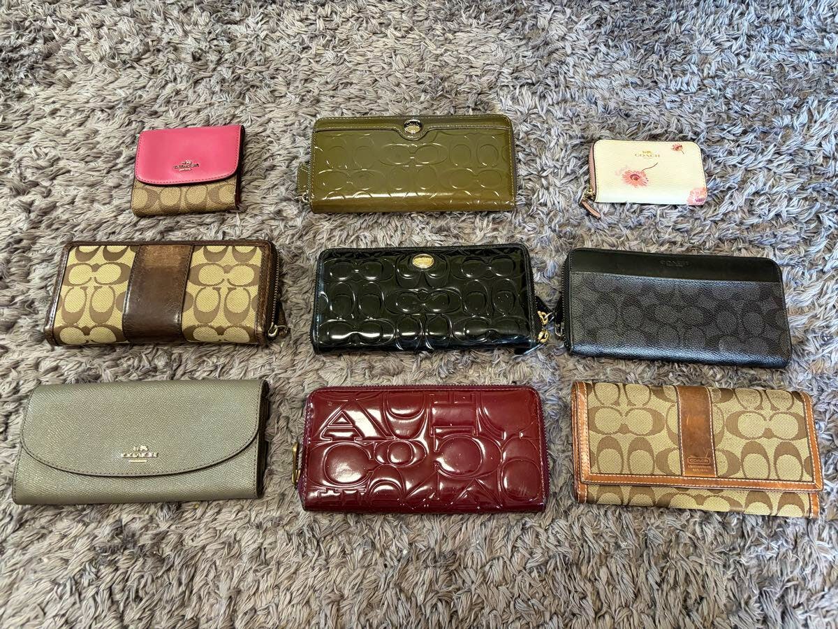 Nine COACH wallets and small wallets in various colors and materials arranged on a gray shag rug.