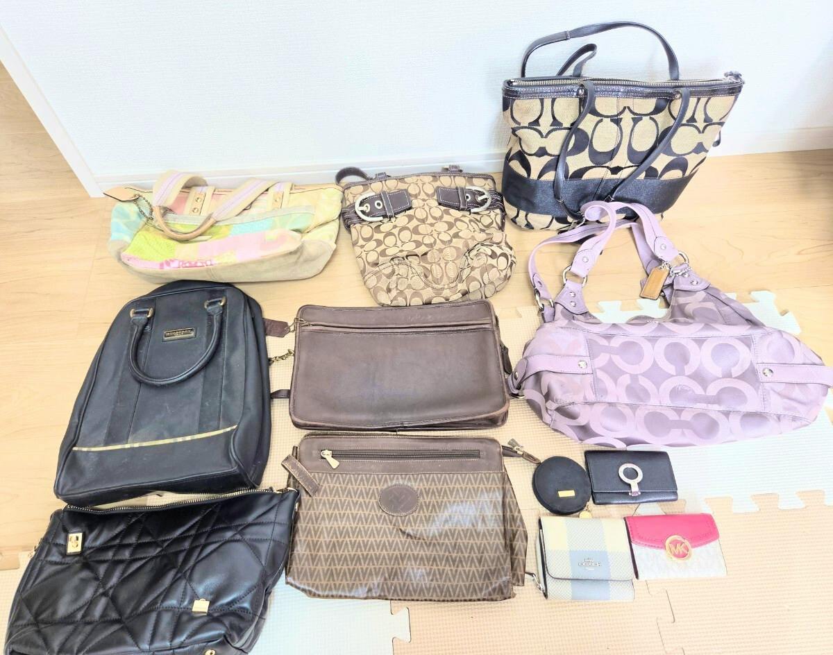 Assorted bags and small accessories, including several Coach signature canvas bags, arranged on a floor.