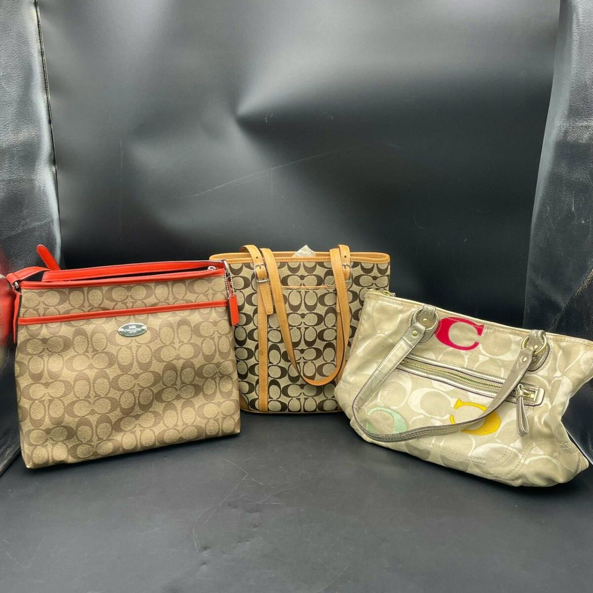 Three Coach beige signature canvas bags (shoulder, hand, and tote) displayed against a black background.