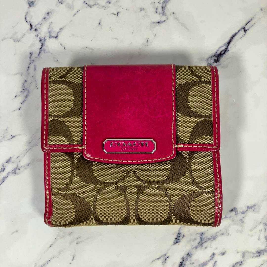 Closed Coach signature canvas bi-fold wallet with pink leather trim and metal logo plate on a marble surface.