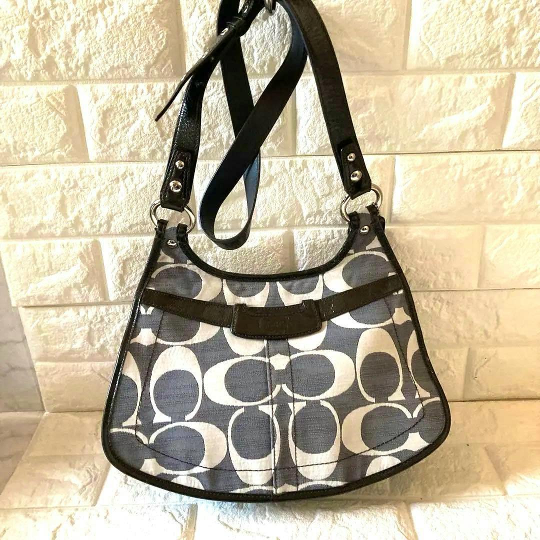 Gray COACH signature canvas shoulder bag with large C pattern and black leather trim hanging against a textured wall.