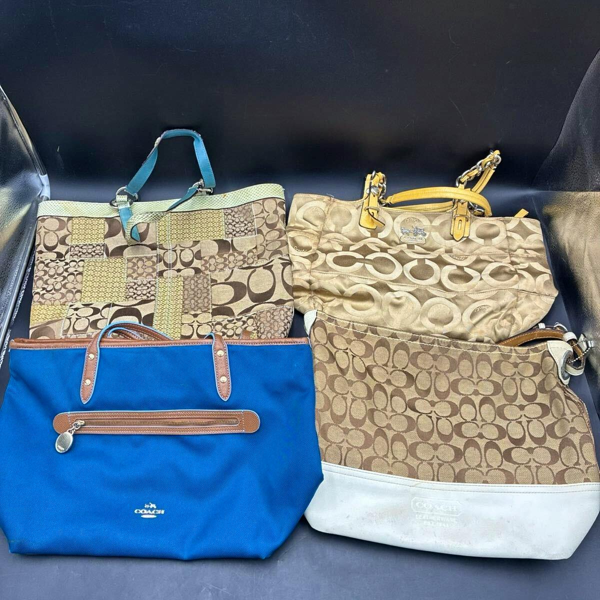 Four Coach tote bags, three brown signature-pattern canvas bags and one blue canvas tote, arranged on a black background.