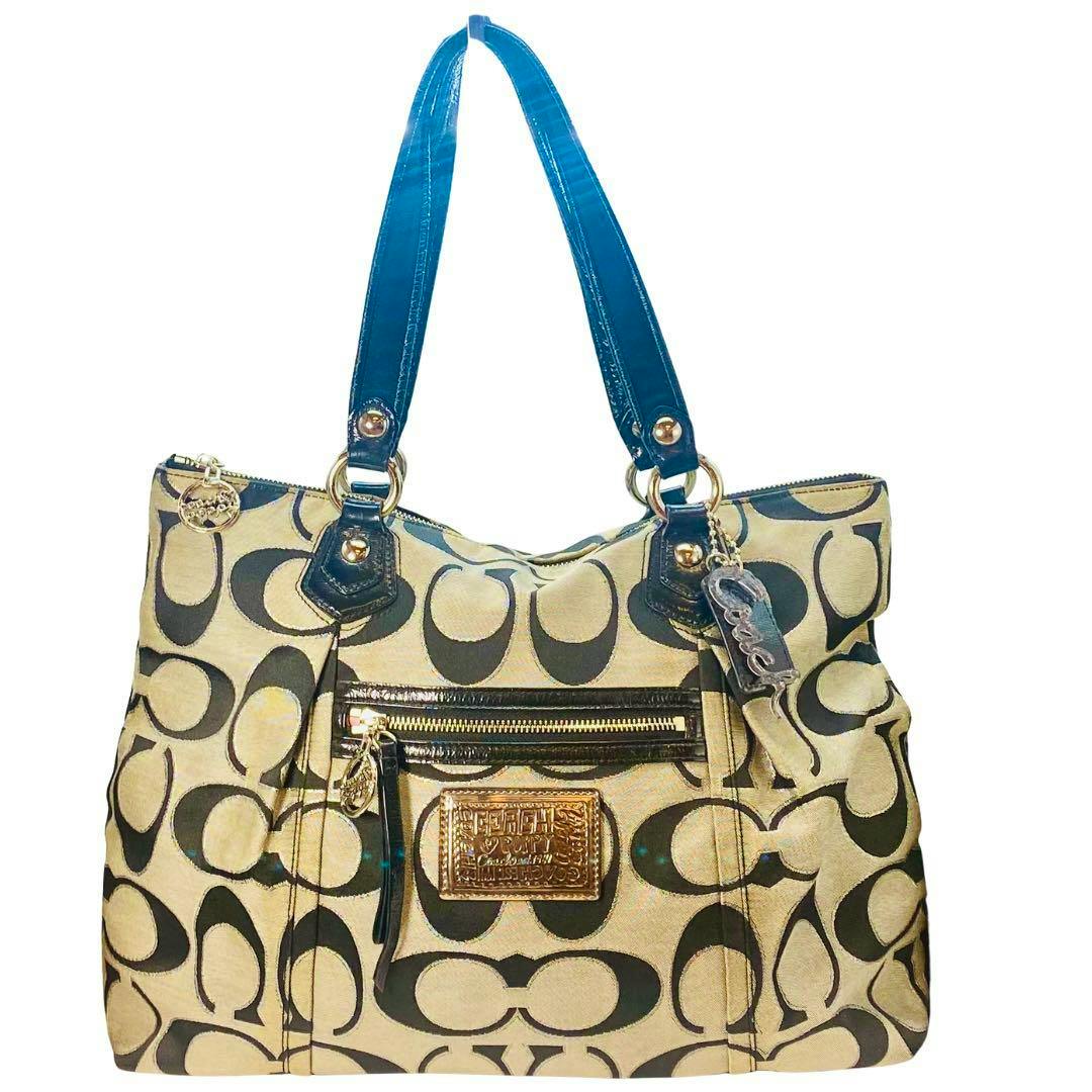Front view of a COACH signature canvas handbag showing the black C‑pattern, dark handles, a front zip pocket, and a metal logo plaque.