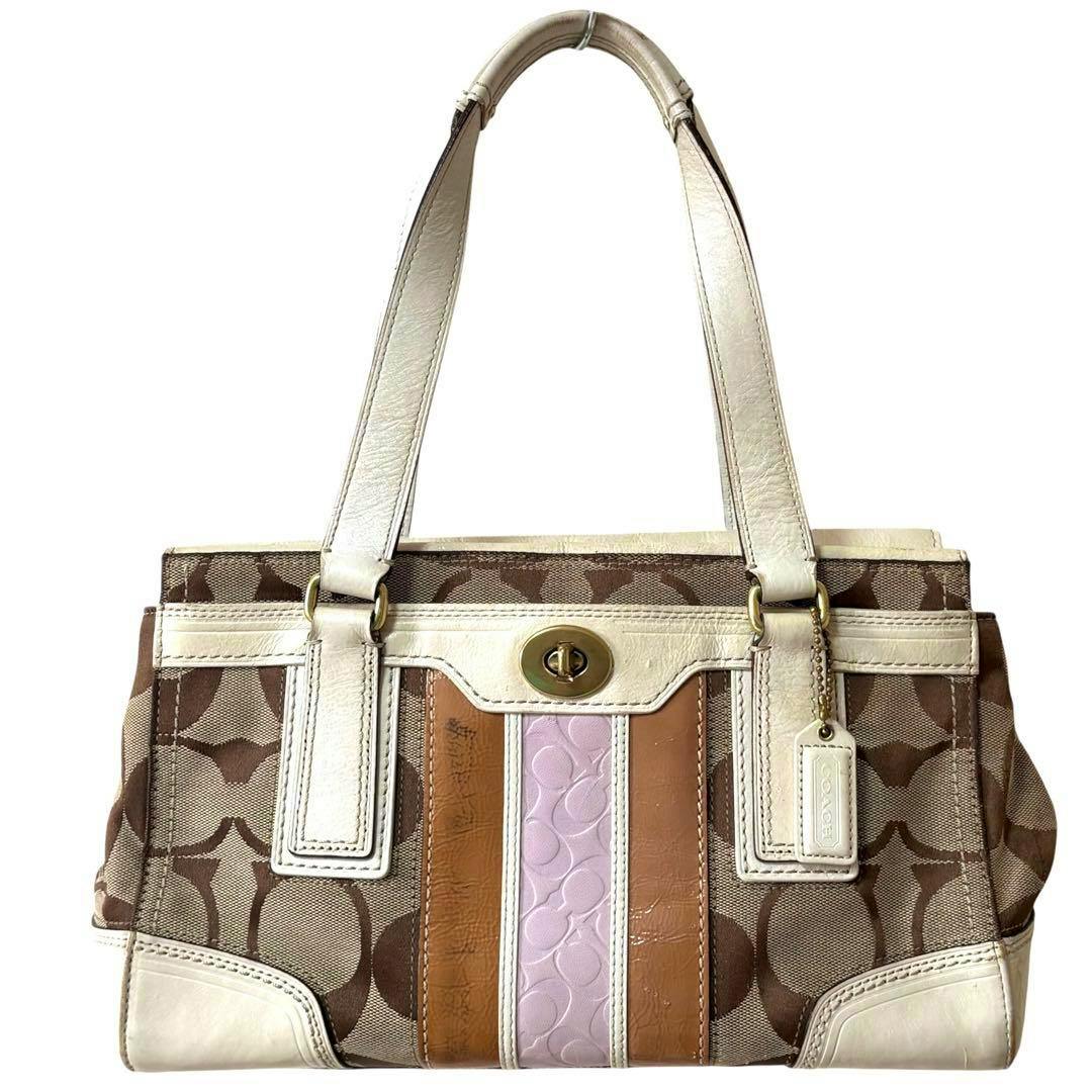 Front view of a COACH signature canvas handbag in brown with white leather trim, tan and light pink center stripes, and white handles.