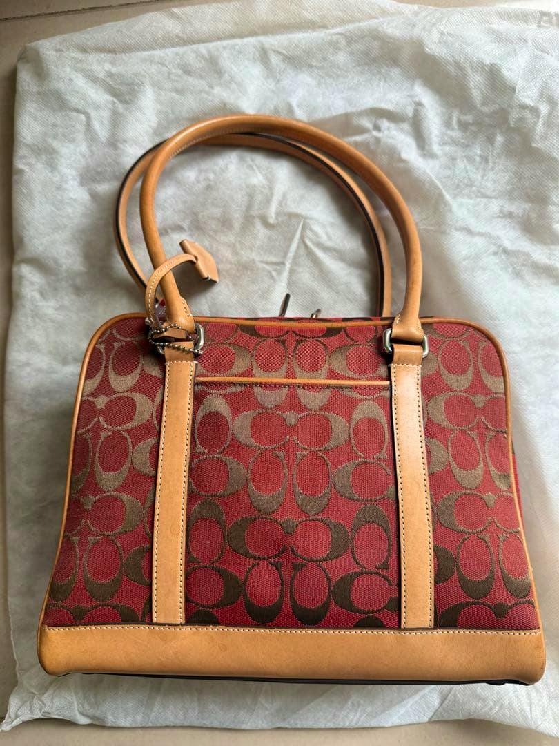 Red COACH signature canvas handbag with tan leather straps and trim photographed flat on a light cloth background.