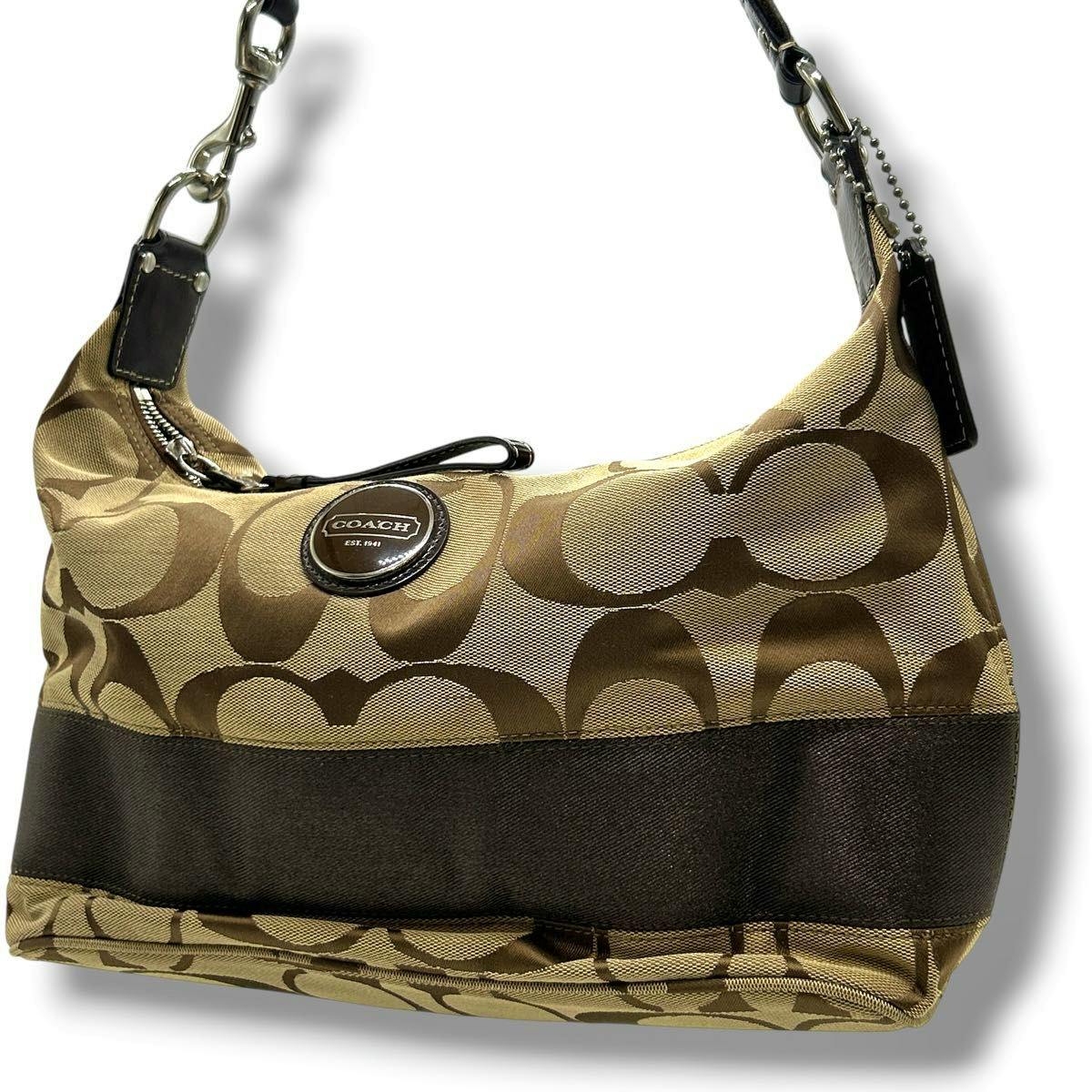 Brown Coach signature canvas and leather shoulder bag with large C pattern and round Coach logo plaque shown against a white background.