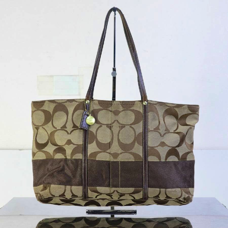 Front view of a brown Coach canvas signature tote bag with leather trim and shoulder straps displayed on a stand.
