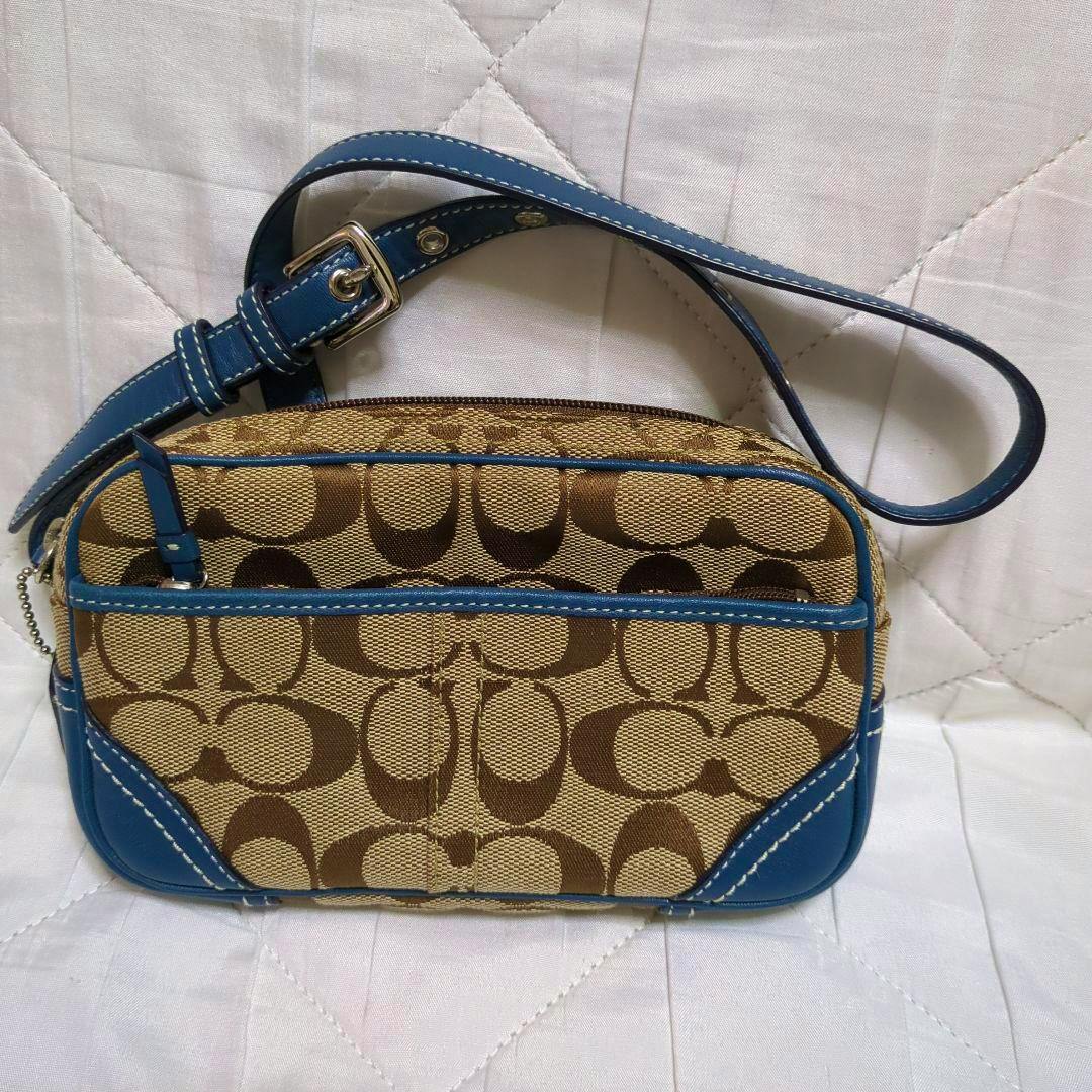 Coach canvas waist pouch with brown signature pattern and blue leather trim and strap on a white quilted background.