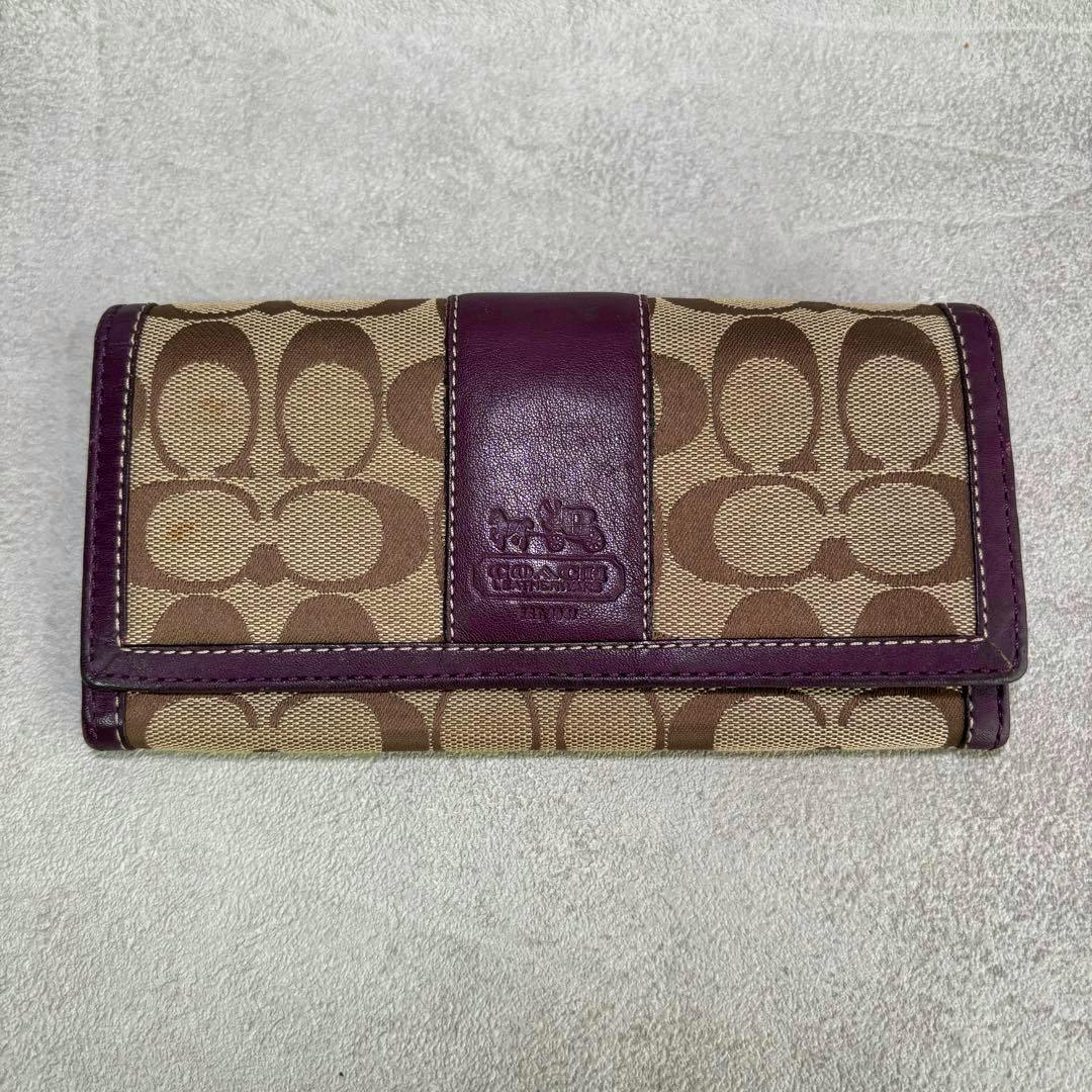 Front view of a Coach long signature canvas wallet in beige with purple leather trim and embossed logo.