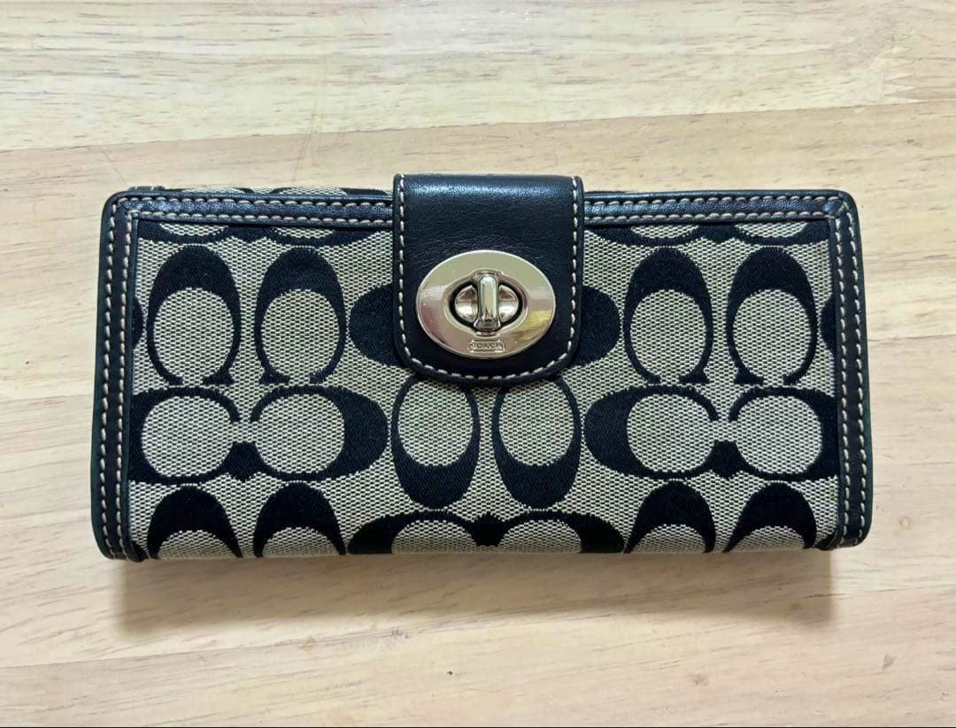 Front view of a black Coach signature canvas long women's wallet with a turn‑lock closure on a wooden surface.