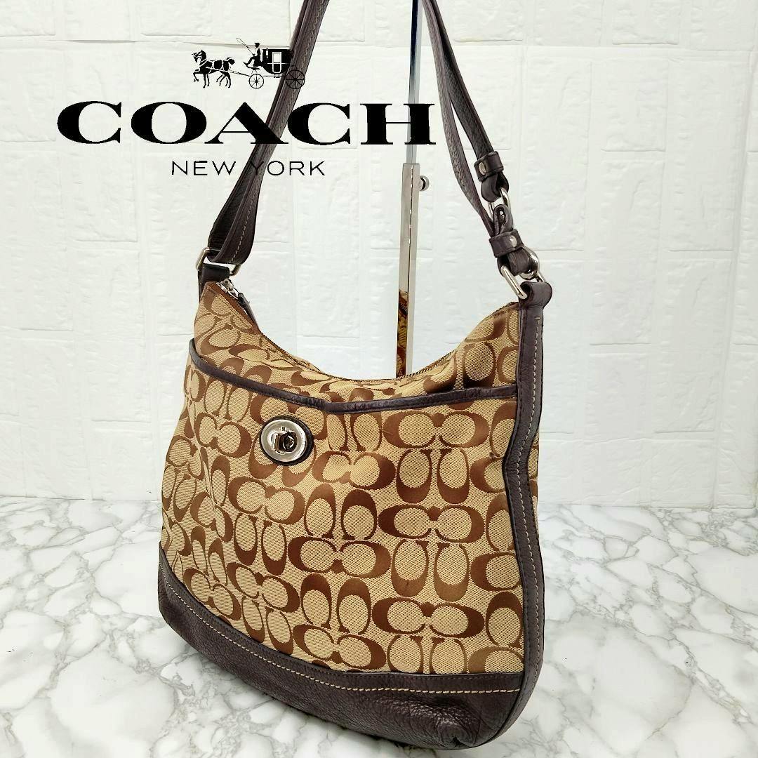 COACH signature canvas one-shoulder bag with turnlock closure displayed on a stand.