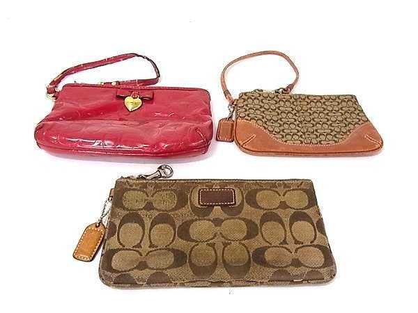 Three COACH pouches — two brown signature canvas pieces and one red patent leather wristlet — displayed on a white background.