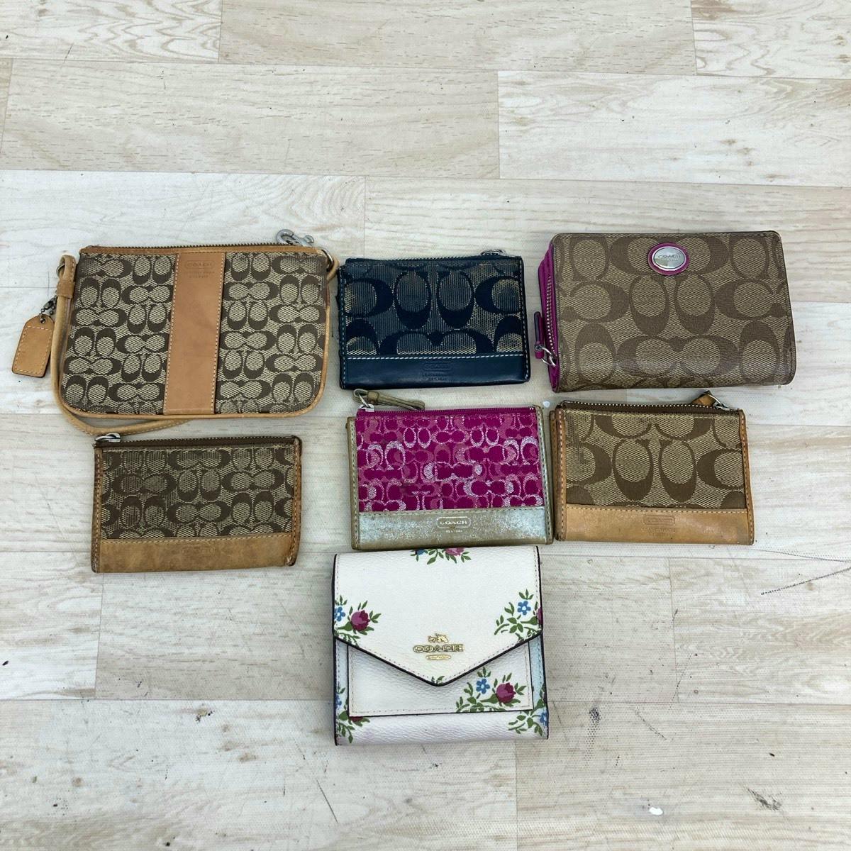 Seven Coach canvas wallets, coin cases, and pouches in signature patterns arranged on a pale wood floor.