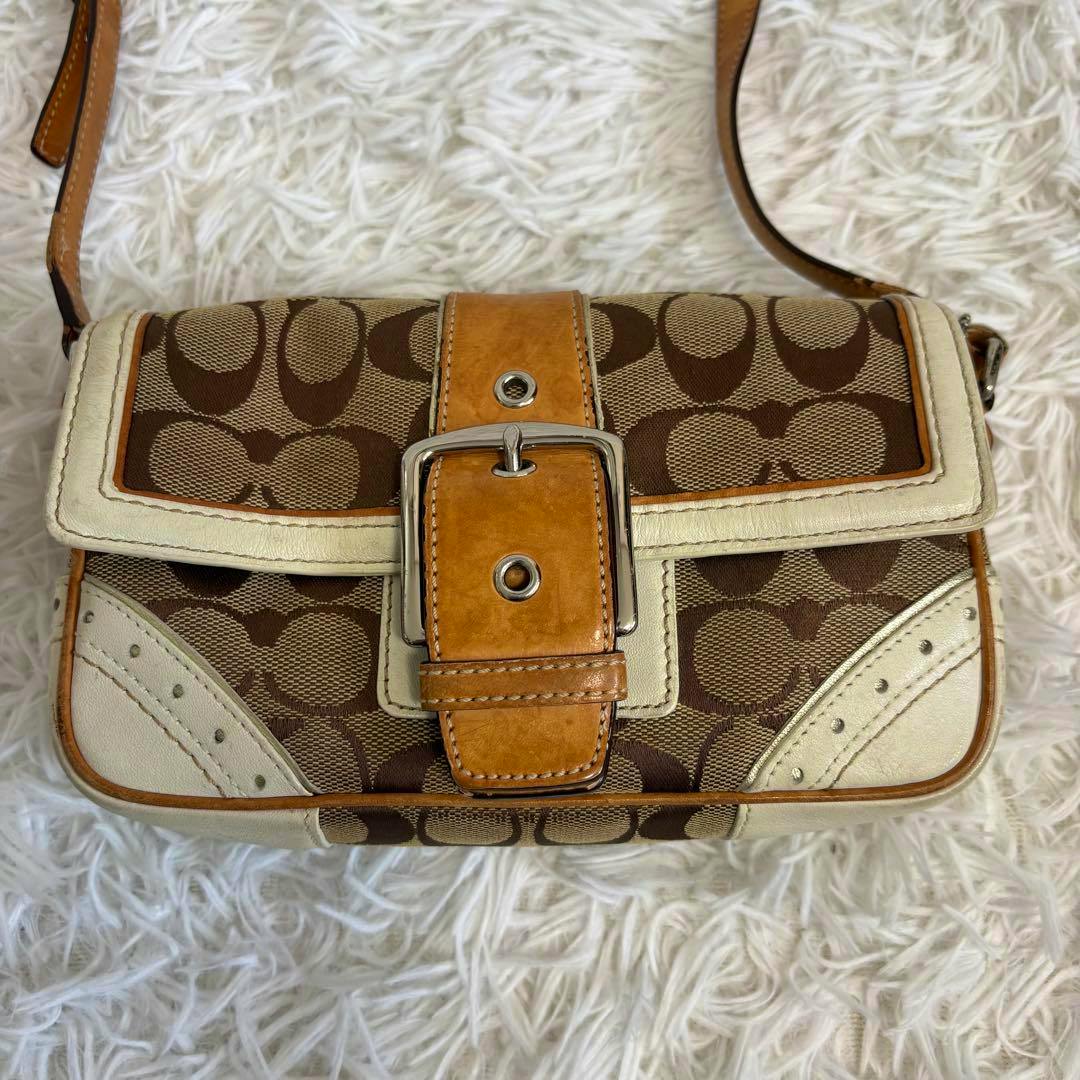Front view of the COACH signature canvas shoulder bag showing the buckle flap and leather trim on a white rug.
