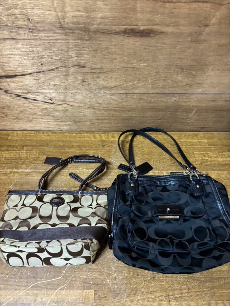 Two COACH signature canvas bags side by side on a wooden surface — a brown/tan signature tote and a black signature shoulder bag.