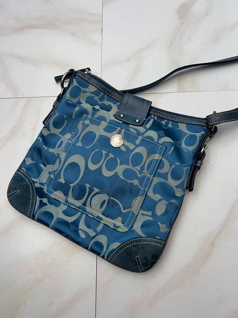 Blue COACH signature canvas shoulder bag with front pocket and leather trim laid on a tiled surface.