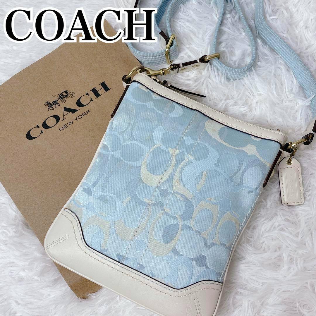 Pastel blue Coach signature canvas shoulder bag with cream leather trim and tag, shown with a Coach box on a white background.
