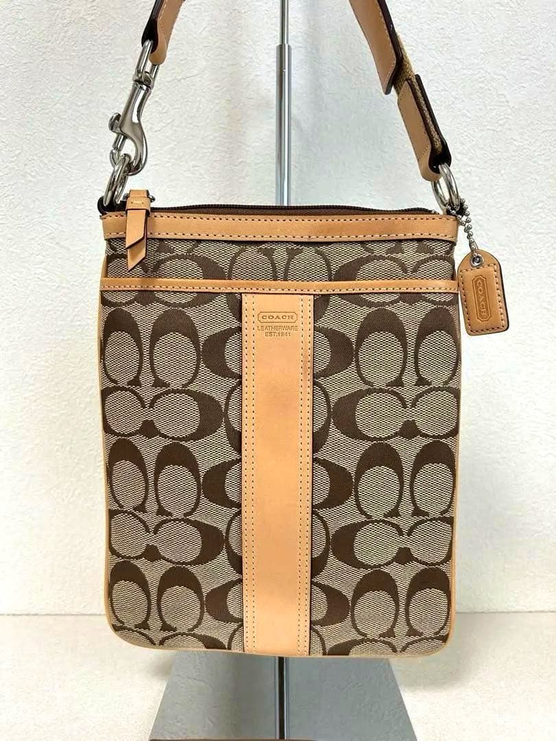 Front view of the Coach signature canvas shoulder sacoche bag with tan leather center stripe and a Coach hang tag.
