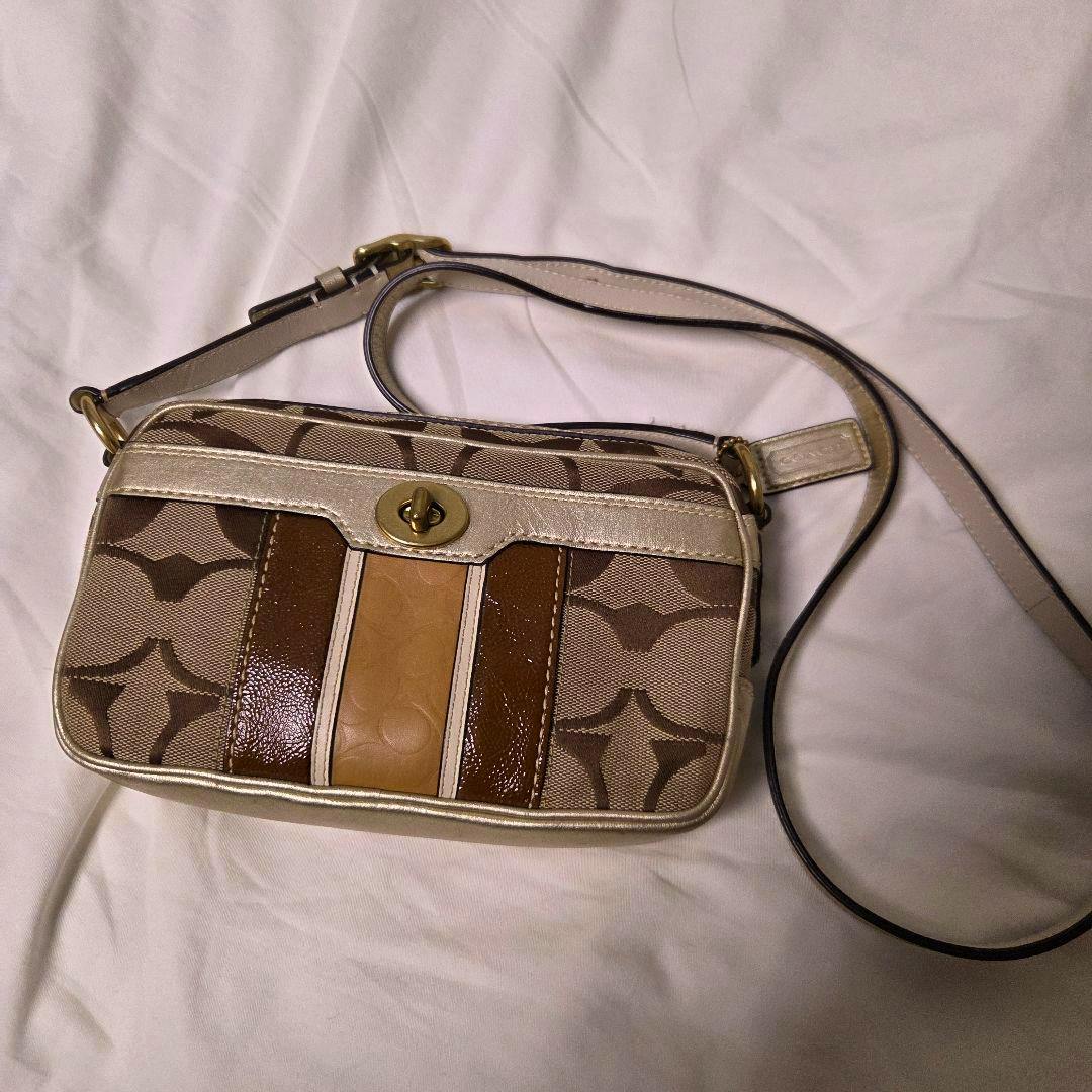 A Coach signature canvas shoulder bag with brown logo pattern, tan and brown leather accents, and a gold turn-lock, shown with its strap on a white background.