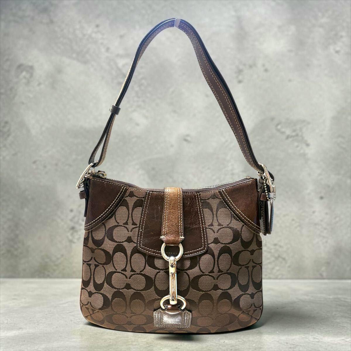 Brown Coach signature canvas shoulder hobo bag with leather trim and metal clasp shown hanging by its strap against a neutral background.