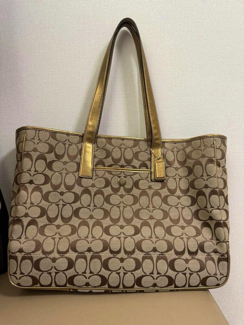 Coach signature canvas tote bag with brown 'C' pattern and gold-tone shoulder straps shown against a light wall.