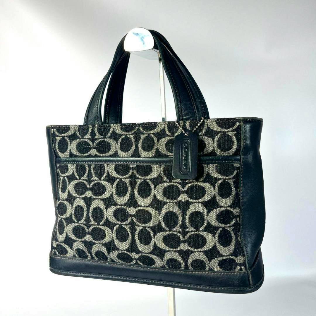 Front view of a COACH signature canvas tote bag with black-and-beige 'C' pattern, black leather trim, and a Coach hang tag.