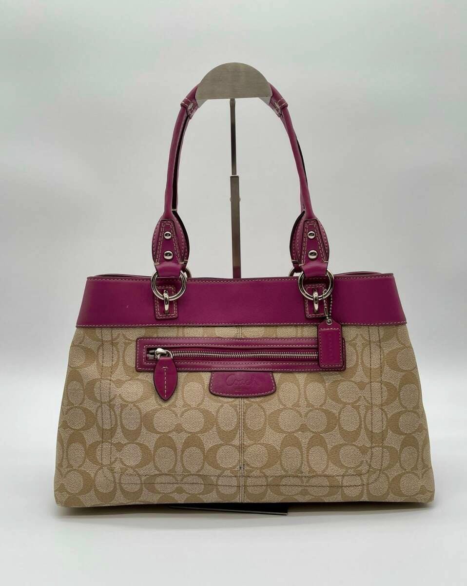 Front view of a COACH canvas signature tote bag in khaki with pink leather trim and double handles displayed on a stand.