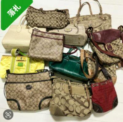 Several COACH signature canvas handbags and small bags arranged together on a white surface.
