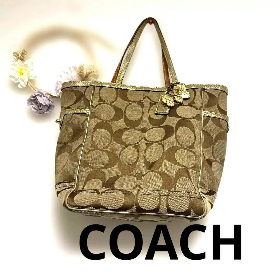 Front view of a COACH signature canvas tote bag with gold trim and a goldfish charm.