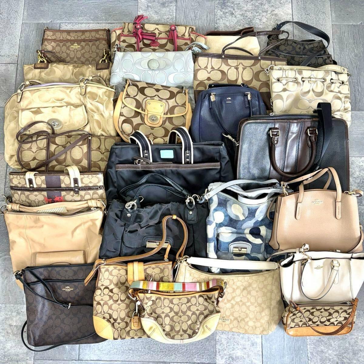 Overhead photo showing a large assortment of Coach bags and purses with signature patterns and various colors arranged on a floor.