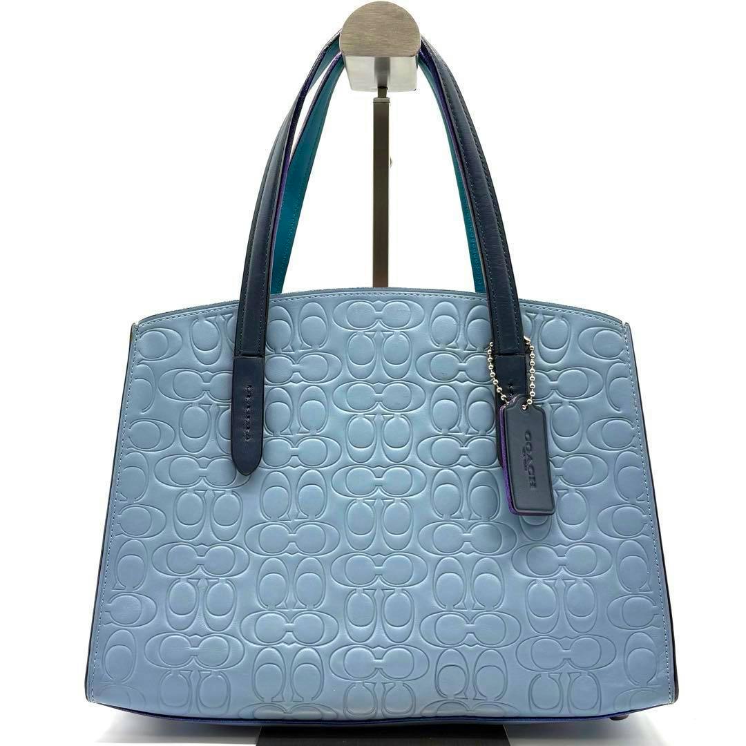 Front view of a light blue Coach embossed leather tote bag with dark handles and a hanging Coach tag.