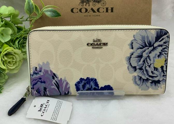 Front view of a COACH long-zip floral canvas women's wallet showing the Coach logo and tag, displayed in front of a Coach box.