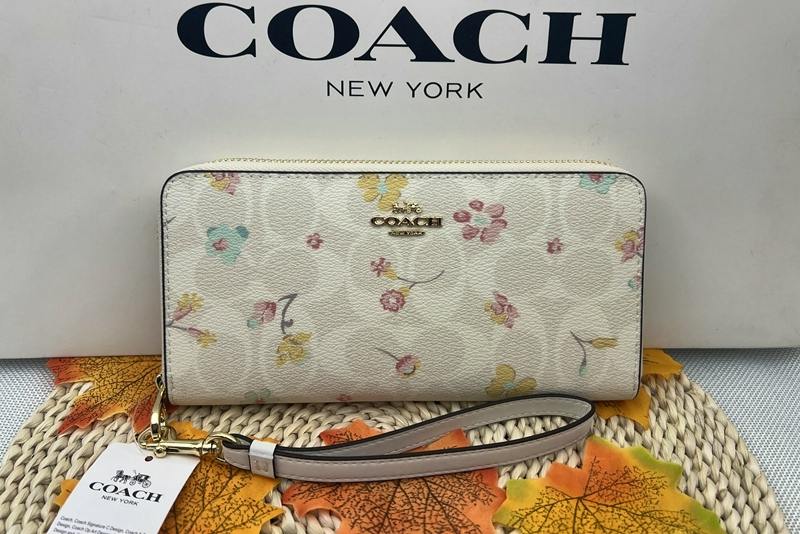 Cream floral COACH long zip-around wallet with wrist strap displayed in front of a COACH box.