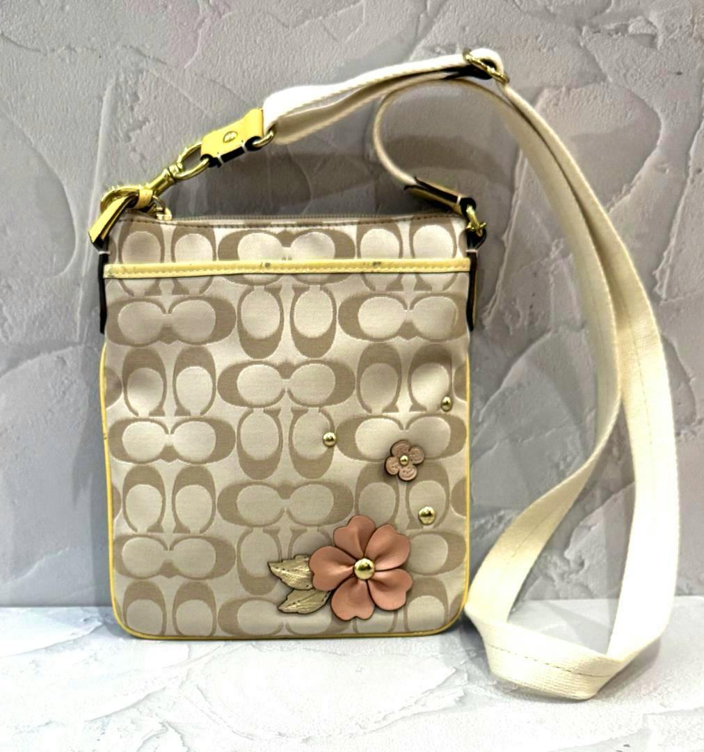 Beige Coach signature canvas shoulder bag with floral appliqué and a cream shoulder strap.