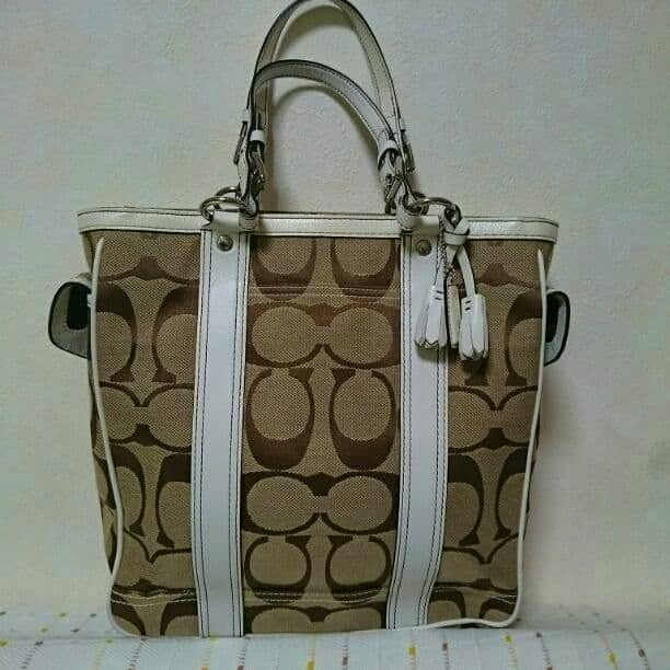 Front view of a Coach signature canvas gallery tote bag with brown signature pattern and white leather trim and handles.