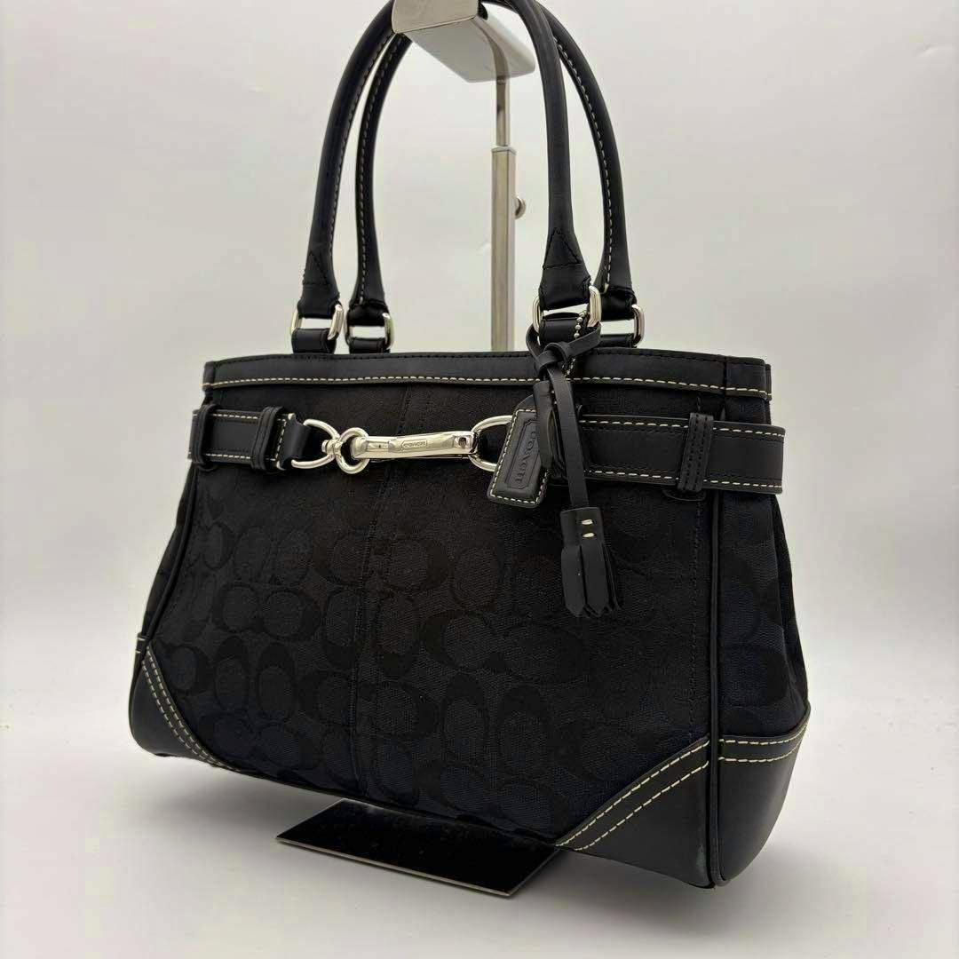 Black Coach signature canvas tote bag with leather trim and silver-tone horsebit detail displayed on a stand.