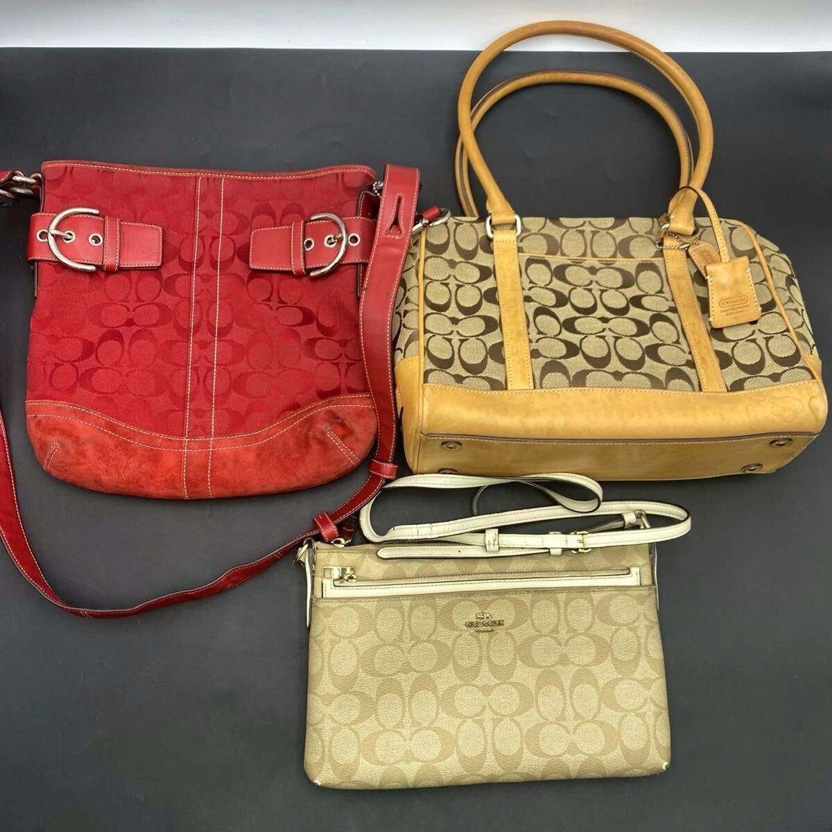 Three COACH bags (a red shoulder bag, a tan signature tote, and a light beige signature crossbody) laid flat on a dark background.
