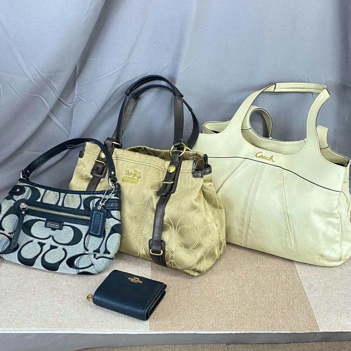 Black Coach bi-fold wallet placed in front of three Coach handbags.