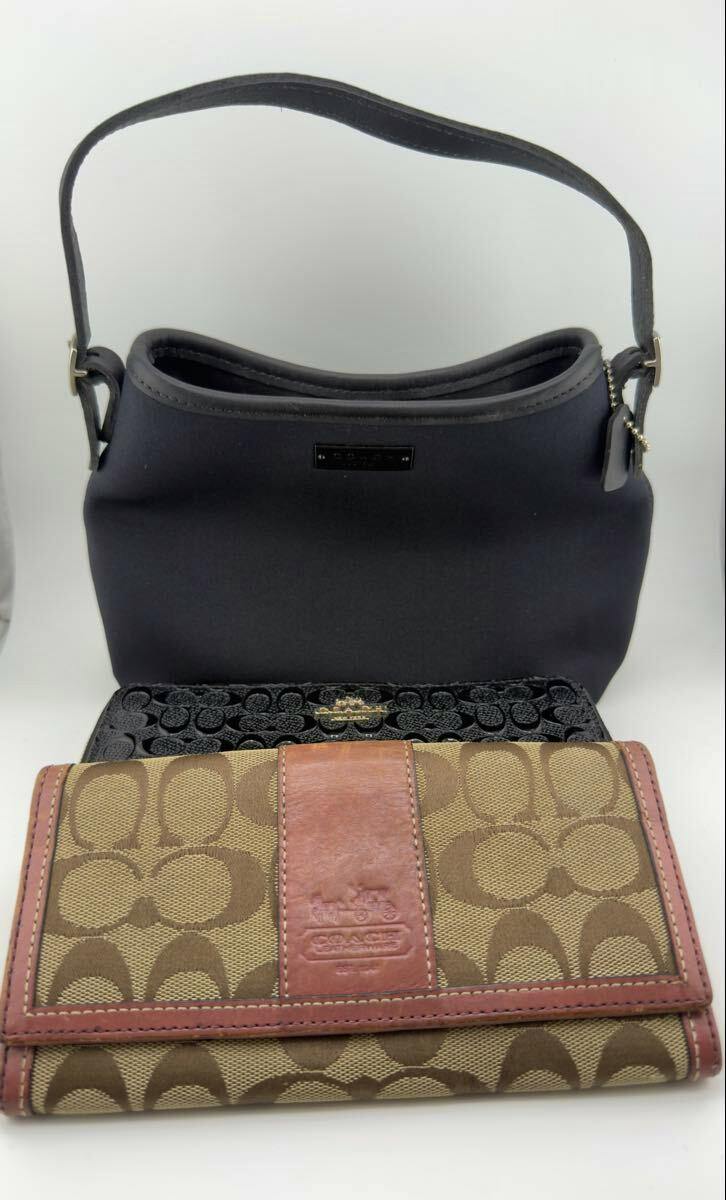 A black Coach handbag is pictured behind two Coach long wallets—one brown signature canvas wallet and one black wallet.